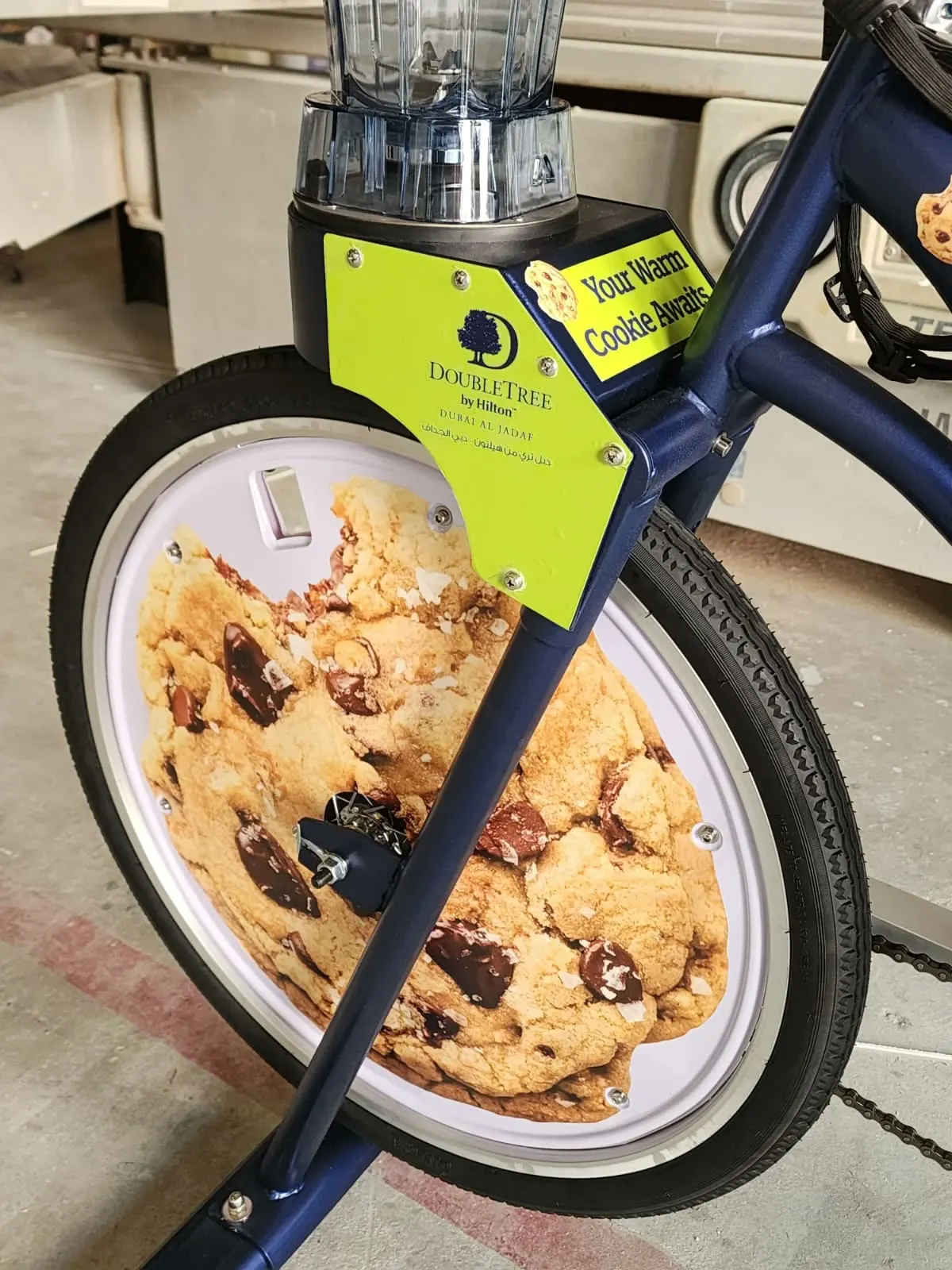 Close-up of the DoubleTree bike's front wheel: chocolate chip cookie printed edge to edge on the disc, lime brand plate above it